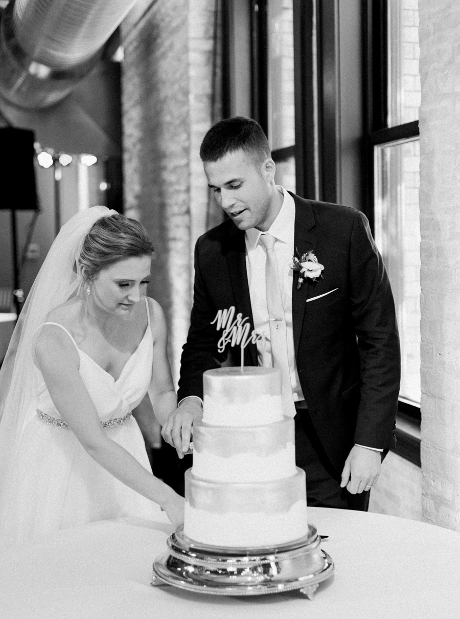 bride and groom cutting cake, Blue Watercolor-Inspired, elegant downtown modern wedding along the Milwaukee River in Wisconsin, photo by Laurelyn Savannah Photography 36
