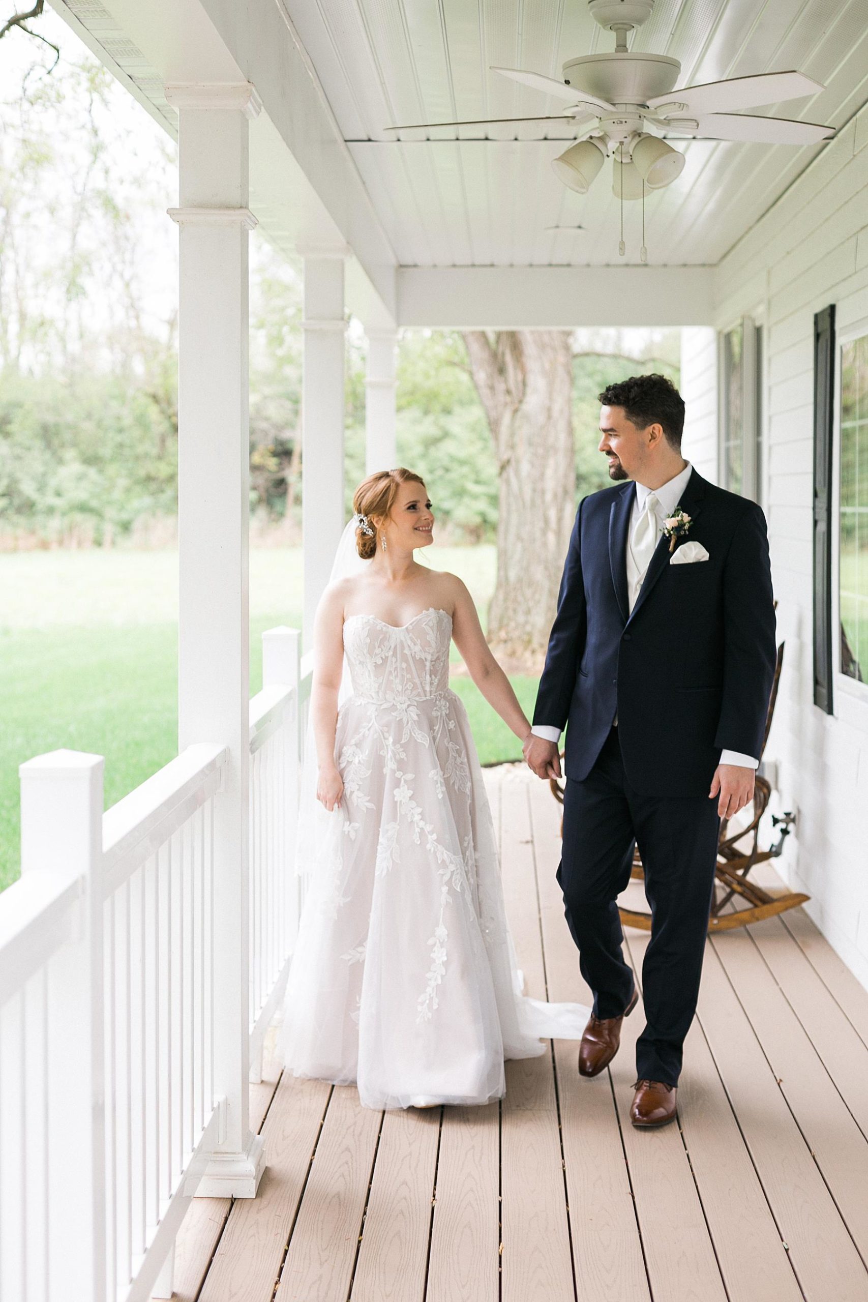 bride and groom walking and holding hands on farmhouse front porch