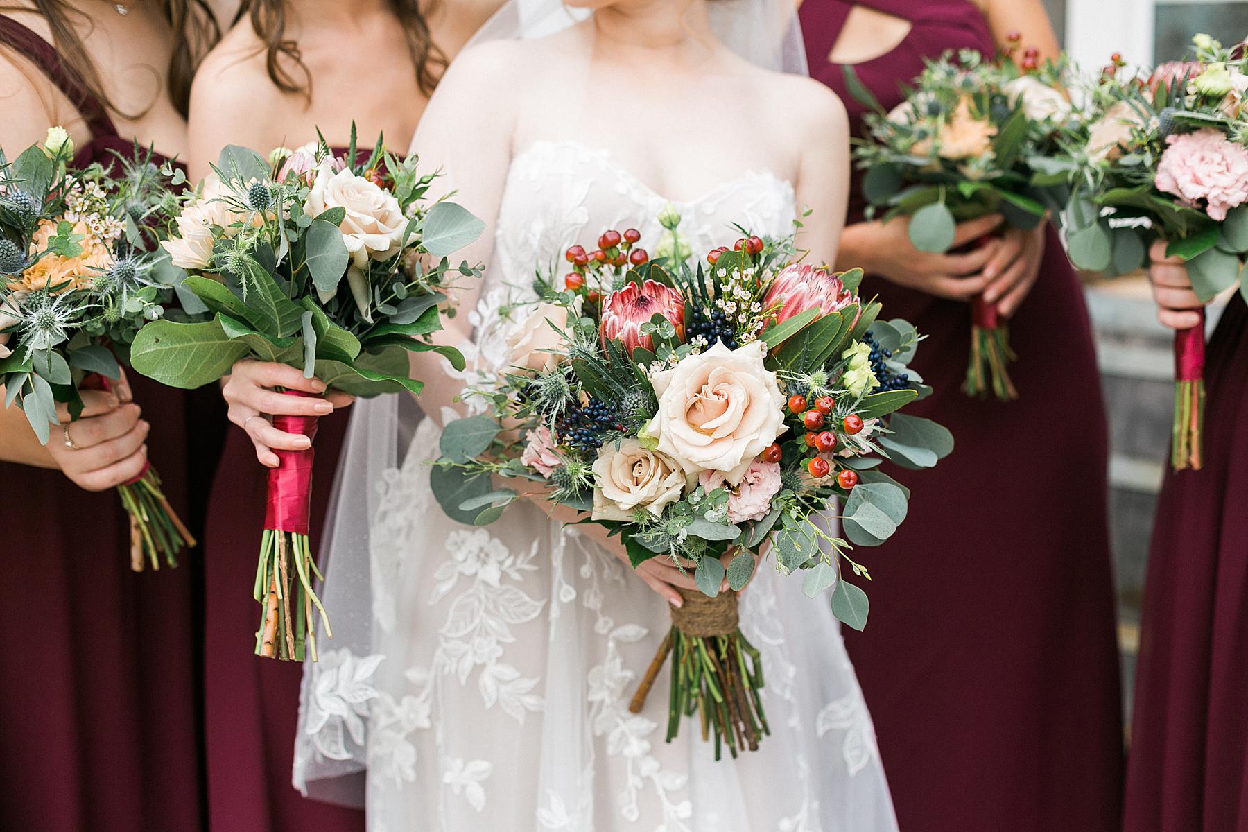 bride holding fall pink and wine red wedding bouquet of flowers at rustic refine barn wedding at lilac acres in milwaukee, wisconsin