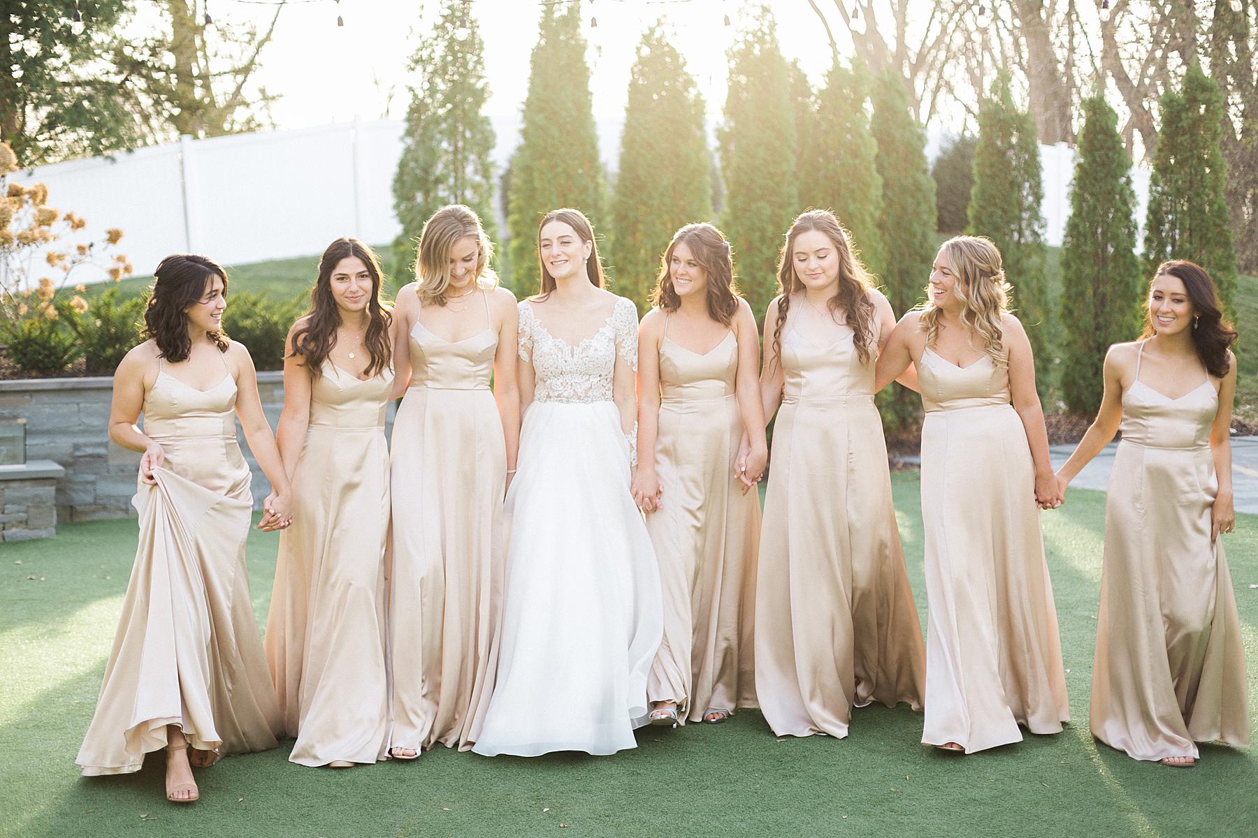 bride in white lace long sleeve gown walking with bridesmaids in nude champagne off-white dresses