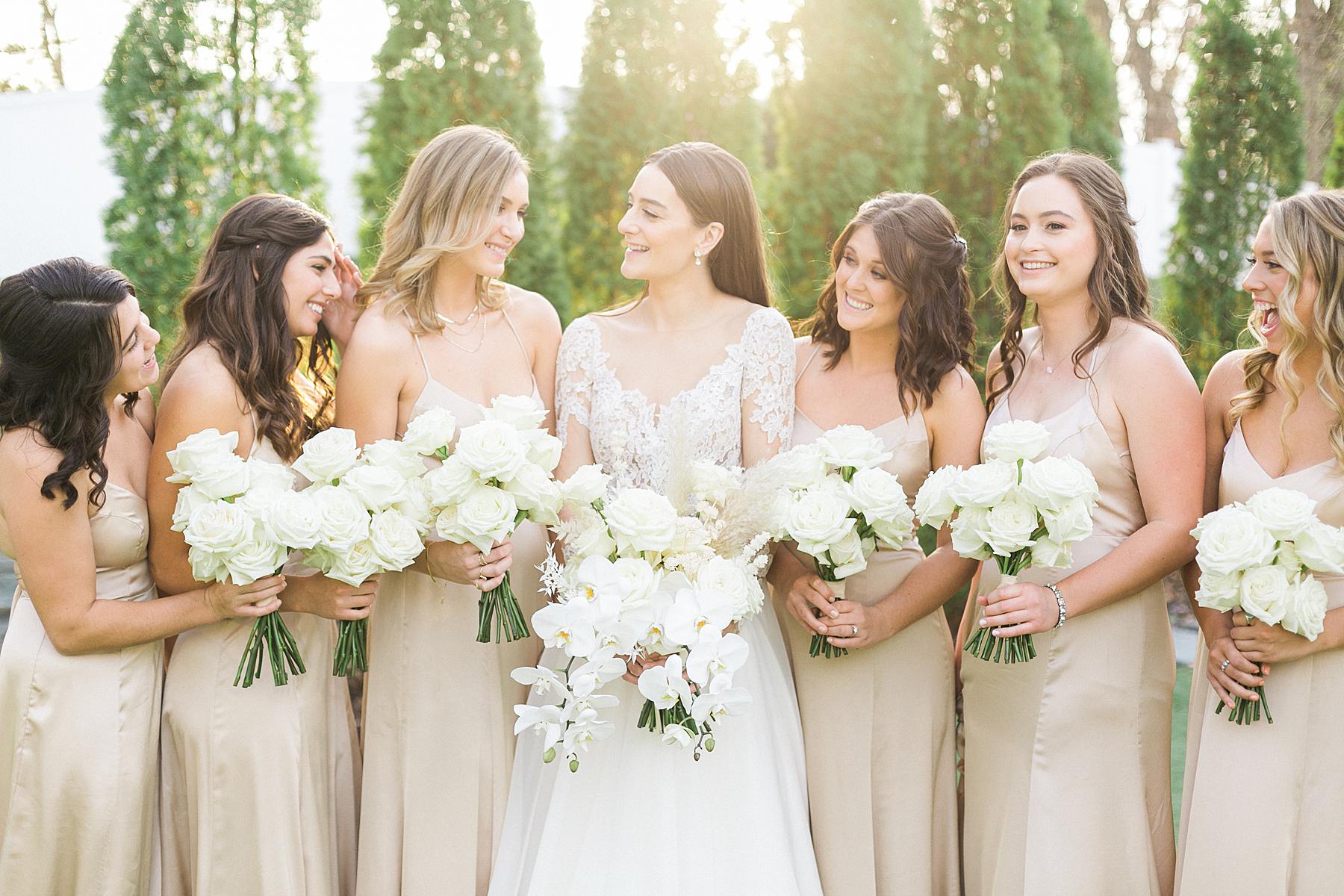 bride in white lace long sleeve gown walking with bridesmaids in nude champagne off-white dresses and white bouquets