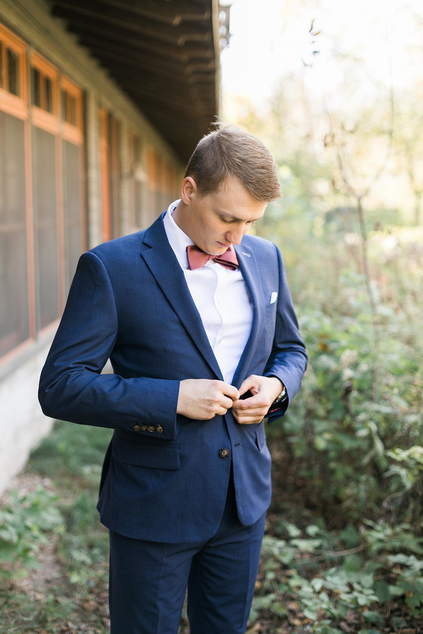 groom getting dressed getting ready in navy blue suit and red bowtie