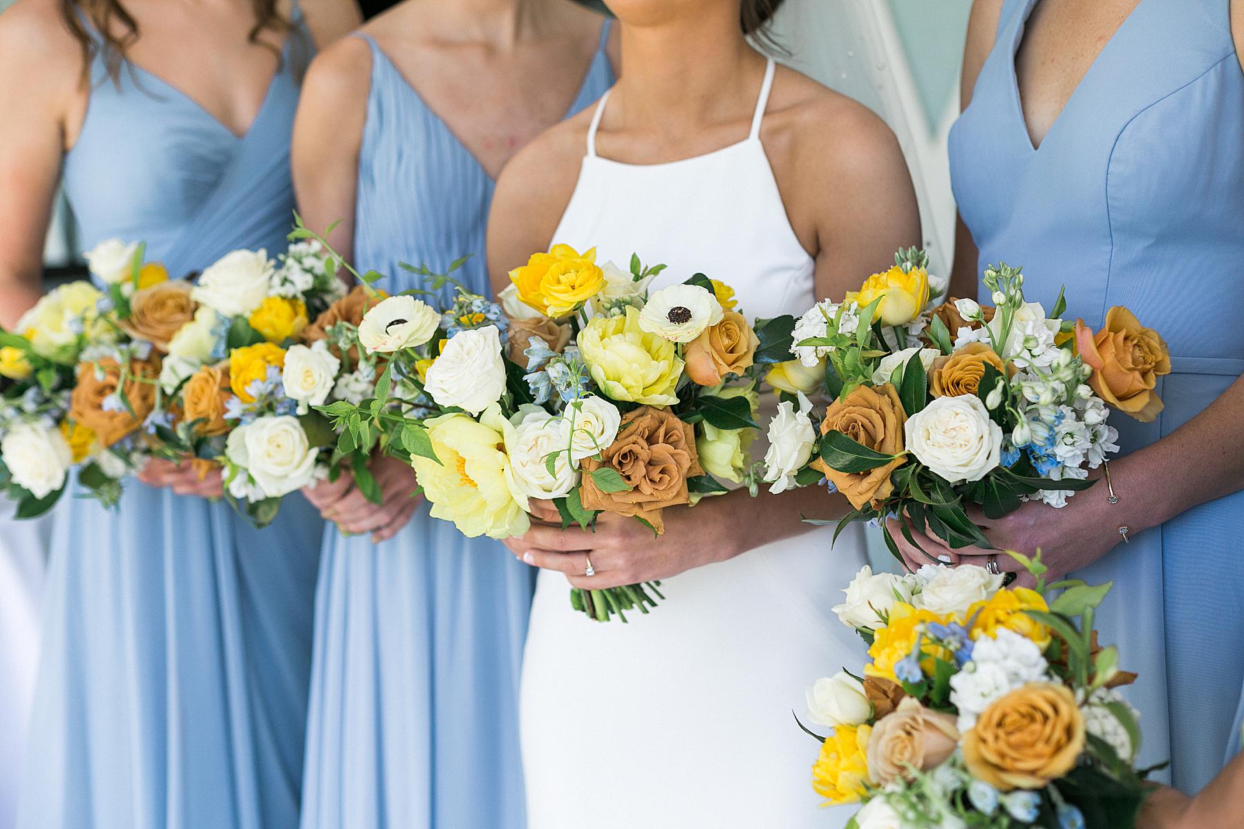 bride and bridesmaid bouquets in yellow, white, and orange, wearing blue dresses