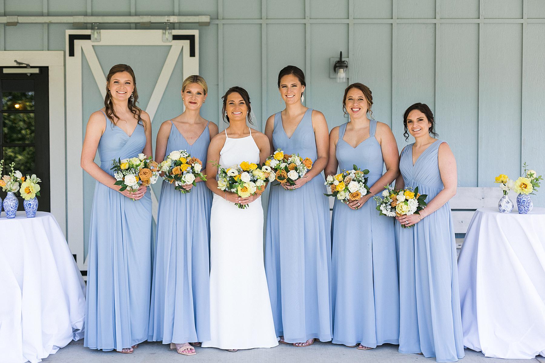 bride and bridesmaid bouquets in yellow, white, and orange, wearing blue dresses